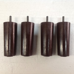 May include: Four dark brown wooden furniture legs with a threaded metal insert at the top. Each leg is approximately 4 inches tall.