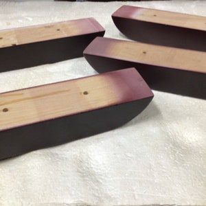 May include: Four dark brown wooden furniture legs with a light brown wood top. The legs are curved and have a rounded shape.
