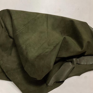 May include: A piece of dark green suede fabric folded in a pile. The fabric has a soft, velvety texture.