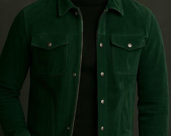 May include: A dark green suede jacket with a zipper closure and two chest pockets. The jacket has a collared neckline and is worn over a black turtleneck. The model is also wearing dark gray pants.
