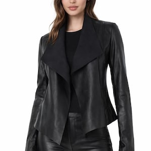 May include: A black leather jacket with a wide collar and long sleeves. The jacket has a tailored fit and a sleek design. The model is wearing black trousers and a black top.