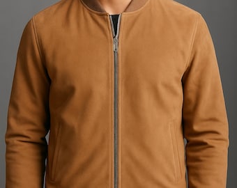 May include: A tan bomber jacket with a full-length zipper, ribbed cuffs, and a ribbed hem. The jacket has two front pockets and a brown collar. The model is wearing a black shirt underneath. The jacket is made of a suede-like material.