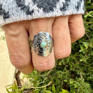 May include: A silver ring featuring a scalloped, circular face with stamped radial patterns and a central, round, light blue and brown matrix turquoise stone. The metal surface displays intricate, repetitive geometric engravings.