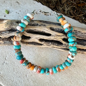 Pode incluir: Uma pulseira de contas redondas e planas em tons de turquesa, branco e laranja. A pulseira &eacute; fixada com um fecho lagosta de metal prateado e pequenos an&eacute;is, exibindo um padr&atilde;o variado de cores de pedra natural em todas as contas.