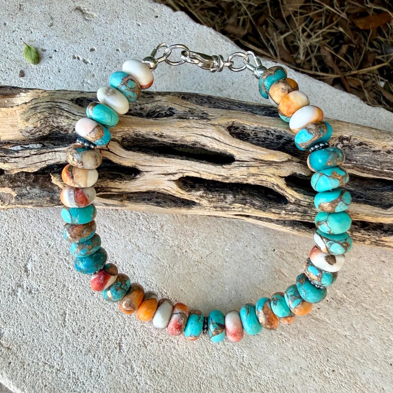 Pode incluir: Uma pulseira de contas redondas e planas em tons de turquesa, branco e laranja. A pulseira &eacute; fixada com um fecho lagosta de metal prateado e pequenos an&eacute;is, exibindo um padr&atilde;o variado de cores de pedra natural em todas as contas.