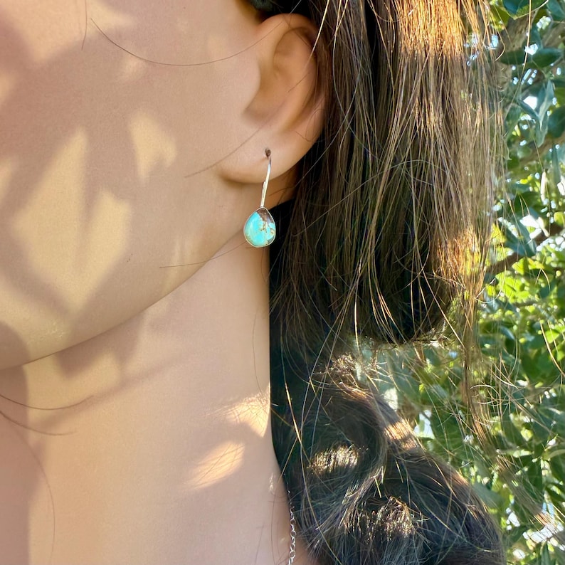 Pu&ograve; includere: Un orecchino pendente in argento con una piccola pietra turchese a forma di goccia, caratterizzata da venature naturali scure. La pietra &egrave; incastonata in una montatura liscia in argento e pende da un semplice gancio sottile in argento.