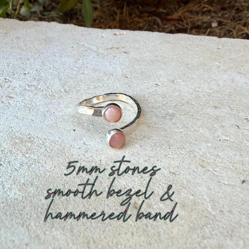 May include: A silver open-style ring featuring two round, light pink stones, each measuring 5mm. The ring has a textured, hammered band and smooth bezels holding the stones in place. The text 5mm stones, smooth bezel & hammered band is visible.