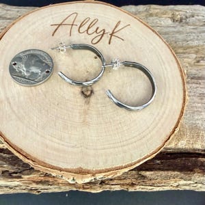 May include: Silver hoop earrings with a textured design, displayed on a wooden slice. A US nickel coin is next to the earrings for size comparison. The wooden slice has the name "Ally K" engraved on it.