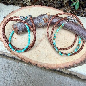 May include: Two wrap bracelets featuring braided brown leather cords and strands of small, round turquoise beads. Each bracelet includes silver-toned metal hardware at the clasp and small silver-toned spacer beads interspersed among the turquoise.