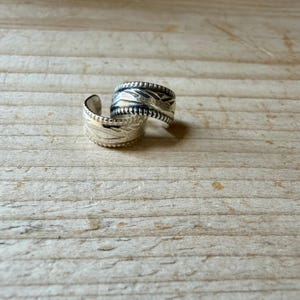 May include: Two silver-toned metal rings with an open-ended design. Each ring features a textured surface with engraved geometric patterns and a beaded border along the edges. The metal has a polished finish with darkened recessed areas.