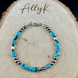 May include: Turquoise and silver beaded bracelet with the text "Allyk" in a handwritten font. The bracelet features oval turquoise stones and small silver beads, connected by a silver clasp. The bracelet is displayed on a wooden surface.