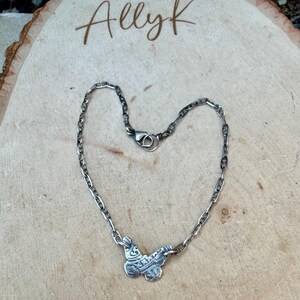 Op de afbeelding: Een zilverkleurige ketting met een vlinderhanger. De ketting heeft een schakelontwerp met een karabijnsluiting. De vlinderhanger heeft ingewikkelde details. Het woord "Allyk" staat in cursief bovenaan.