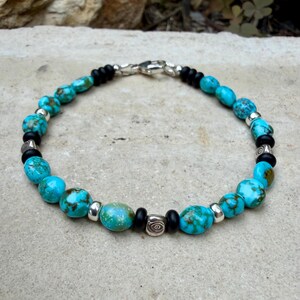 May include: Turquoise and black beaded bracelet with silver accents. The bracelet features round, turquoise beads interspersed with black beads and silver-toned metal spacers. A silver clasp secures the bracelet.