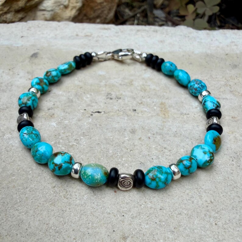 May include: Turquoise and black beaded bracelet with silver accents. The bracelet features round, turquoise beads interspersed with black beads and silver-toned metal spacers. A silver clasp secures the bracelet.