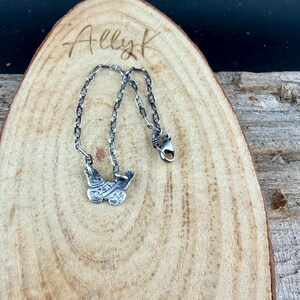 Op de afbeelding: Een zilveren vlinderhanger ketting met een ketting. De vlinderhanger heeft ingewikkelde ge&euml;tste details. De ketting wordt weergegeven op een houten oppervlak met de handgeschreven tekst "Ally K".