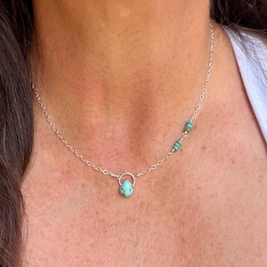 May include: A delicate silver chain necklace featuring a single teardrop-shaped turquoise pendant suspended from a small circular silver loop. The chain includes two additional small turquoise beads positioned asymmetrically along the right side.