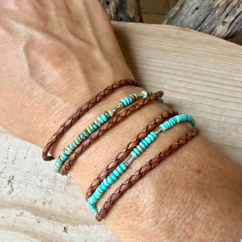 May include: A multi-strand bracelet featuring two braided brown leather cords and two rows of beads. One row contains variegated turquoise-colored stone beads with silver spacers, while the other row features bright turquoise beads with silver accents.