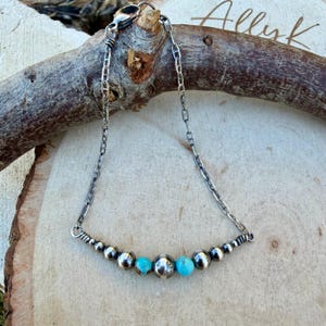 Peut inclure: Un collier en argent avec une cha&icirc;ne et une rang&eacute;e de perles argent&eacute;es et turquoises. Le collier est pr&eacute;sent&eacute; sur un morceau de bois. Le mot "Allyk" est &eacute;crit en cursive sur le bois.