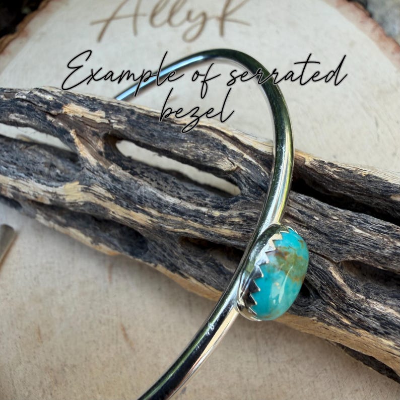 K&ouml;nnte beinhalten: Ein silberfarbenes Armband mit einem T&uuml;rkisstein, der in einer gezahnten L&uuml;nette gefasst ist. Das Armband ist gebogen und tr&auml;gt den Text "Example of serrated bezel" in Kursivschrift. Der Hintergrund ist ein St&uuml;ck Holz.