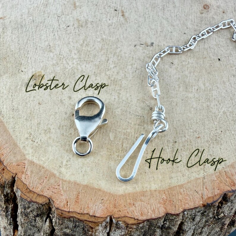 May include: Close-up of two types of jewelry clasps: a silver lobster clasp and a hook clasp. The clasps are on a wooden surface. The words "Lobster Clasp" and "Hook Clasp" are written in cursive.