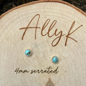 May include: Two small turquoise stud earrings with a serrated edge, each 4mm in diameter, are displayed on a wooden surface. The word "Allyk" is written in a cursive font above the earrings, and the text "4mm serrated" is below.