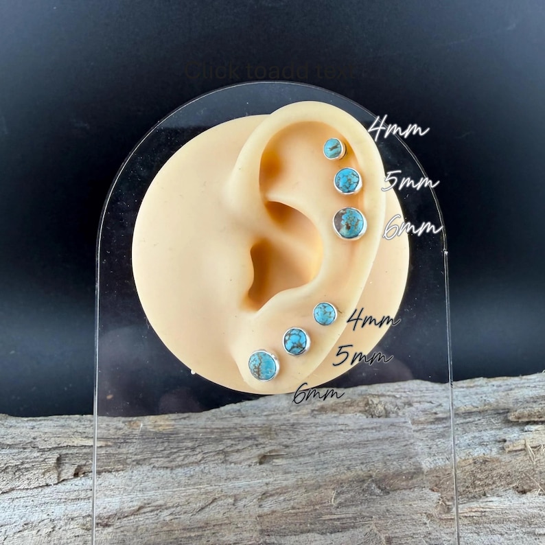 May include: A display of turquoise stud earrings in various sizes, including 4mm, 5mm, and 6mm. The earrings are set in silver and are shown on a model ear. The background is dark, and the earrings are displayed on a clear acrylic stand.