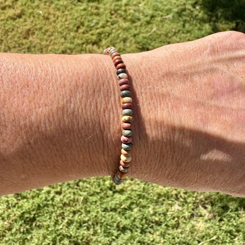 May include: A beaded bracelet with a variety of earth-toned beads, including shades of red, brown, green, and yellow. The bracelet is strung on a flexible cord and is worn on a wrist. The bracelet is a simple, yet elegant piece of jewelry.
