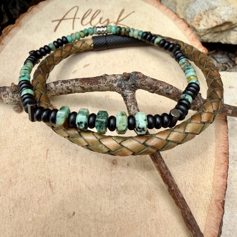 May include: Two bracelets are displayed. One is a braided brown leather bracelet. The other is a beaded bracelet with black and turquoise beads. The bracelets are on a wooden surface with the word "Allyk" in cursive.
