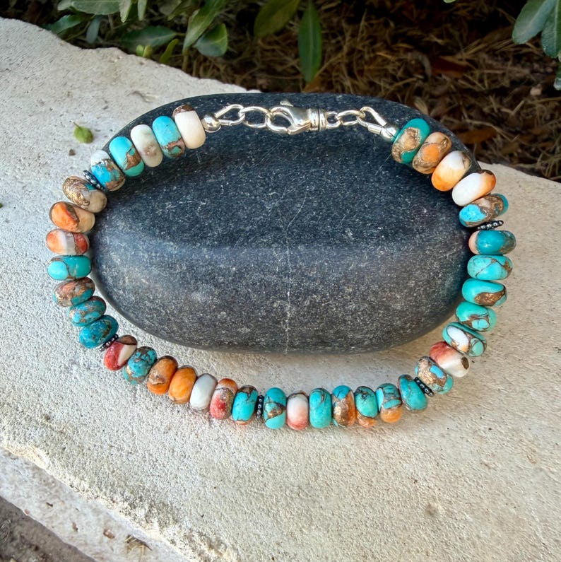 Pode incluir: Uma pulseira de contas com pedras redondas e achatadas em tons de turquesa, laranja e branco com padr&otilde;es de matriz castanha. As contas est&atilde;o enfiadas e presas com um fecho de lagosta e um anel de liga&ccedil;&atilde;o em metal prateado.