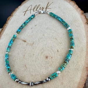 Pu&ograve; includere: Collana di perline turchesi con dettagli argentati. La collana presenta piccole perline rotonde turchesi in tonalit&agrave; blu e verde, infilate con perline di metallo argentato e una chiusura. La collana &egrave; esposta su una superficie di legno.