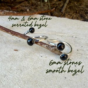 May include: Two silver rings with black stones resting on a wooden branch. One ring features a 4mm stone in a serrated bezel, while the other displays a 6mm stone in a smooth bezel. Text on the image reads 4mm & 6mm stone serrated bezel and 6mm stones smooth bezel.
