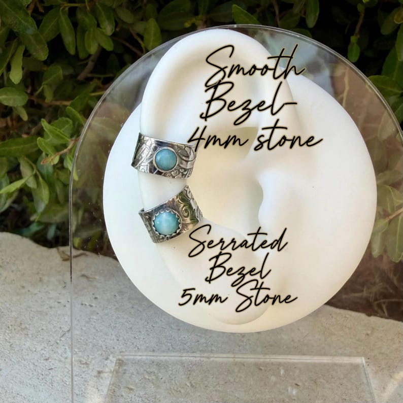 May include: Two silver ear cuffs with patterned bands and light blue stones. The top cuff features a smooth bezel with a 4mm stone. The bottom cuff features a serrated bezel with a 5mm stone. The text on the display reads Smooth Bezel 4mm stone and Serrated Bezel 5mm Stone.