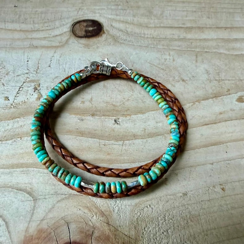 May include: A bracelet featuring a braided brown leather cord intertwined with a strand of small, round, turquoise-colored beads. The piece is secured with a silver-toned metal lobster claw clasp and jump ring closure, creating a layered look.