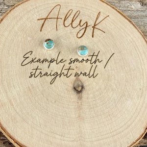May include: Two small turquoise and silver stud earrings on a wooden surface. The earrings have a round turquoise stone set in a silver bezel. The wooden surface has the name "Allyk" and the text "Example smooth / straight wall" written on it.