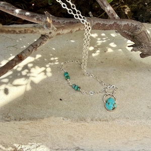 May include: A silver chain necklace featuring a teardrop-shaped turquoise pendant and small turquoise beads integrated into the chain links. The necklace has a metallic silver finish and displays natural blue-green stone variations throughout.
