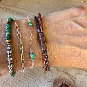 Puede incluir: Un conjunto de cuatro pulseras que incluye una con cuentas de turquesa y esferas plateadas, una cadena de eslabones ovalados dorados, una cadena fina de plata con tres cuentas de turquesa y un cord&oacute;n de cuero trenzado marr&oacute;n con cierre.