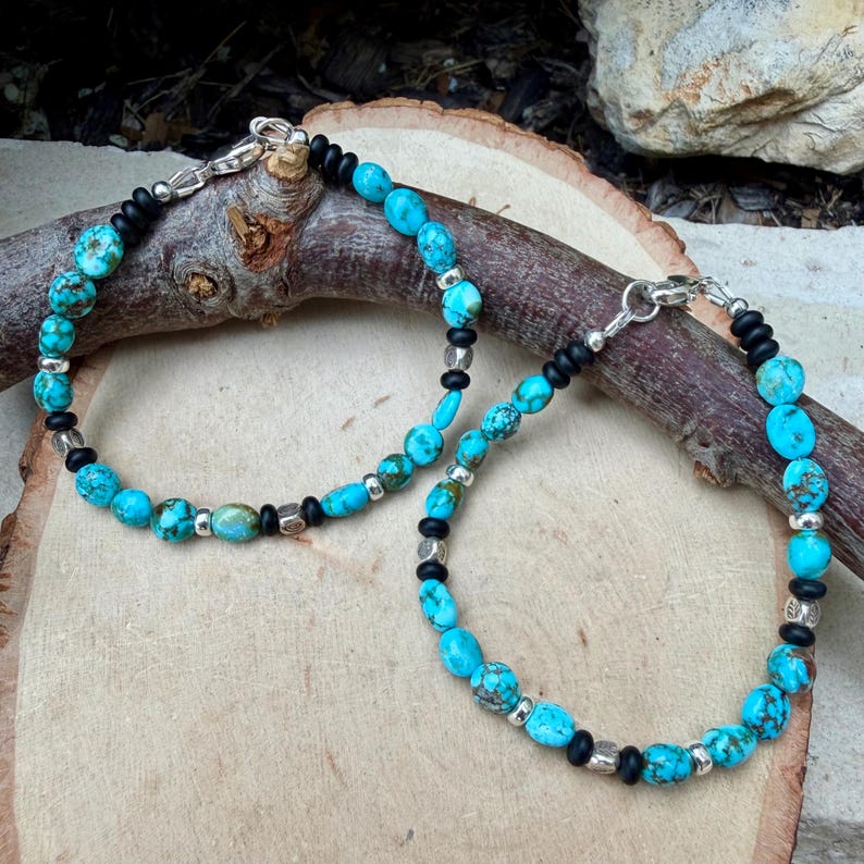 May include: Two turquoise beaded bracelets with black and silver accents. The bracelets feature round and oval turquoise beads, interspersed with black beads and silver-colored metal spacers. Each bracelet has a silver clasp.
