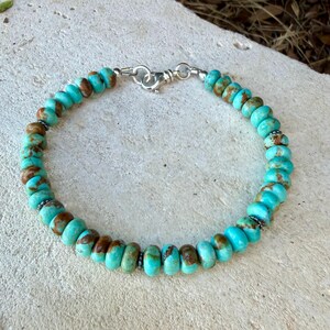 May include: A beaded bracelet featuring round, disc-shaped turquoise stones with natural brown matrix patterns. The beads are strung together and secured with a polished silver-toned metal lobster claw clasp and a circular jump ring connector.