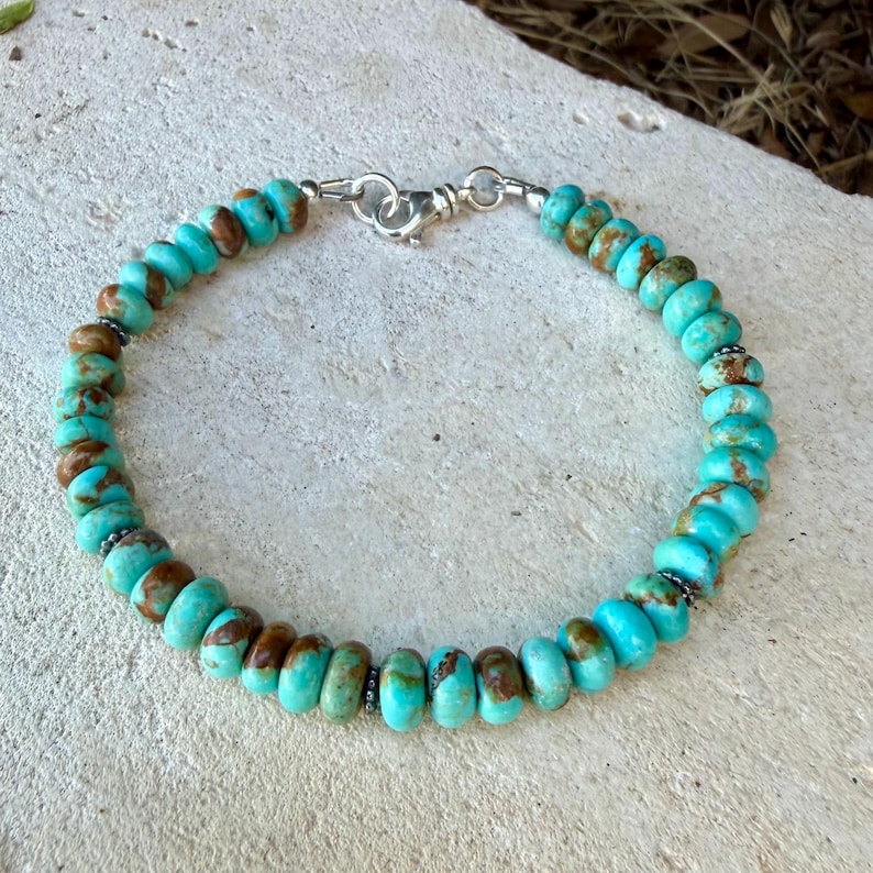 May include: A beaded bracelet featuring round, disc-shaped turquoise stones with natural brown matrix patterns. The beads are strung together and secured with a polished silver-toned metal lobster claw clasp and a circular jump ring connector.