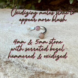 May include: A silver open ring featuring two round blush-colored stones, one 4mm and one 5mm, set in serrated bezels. The band has a hammered and oxidized finish. Text on image: Oxidizing mutes stone to appear more blush. 4mm & 5mm stone with serrated bezel hammered & oxidized.