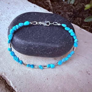 May include: A bracelet featuring small, irregular, bright turquoise-colored stone beads interspersed with thin, cylindrical silver-toned metal spacers. The piece is secured with a silver-toned lobster claw clasp and jump ring closure.