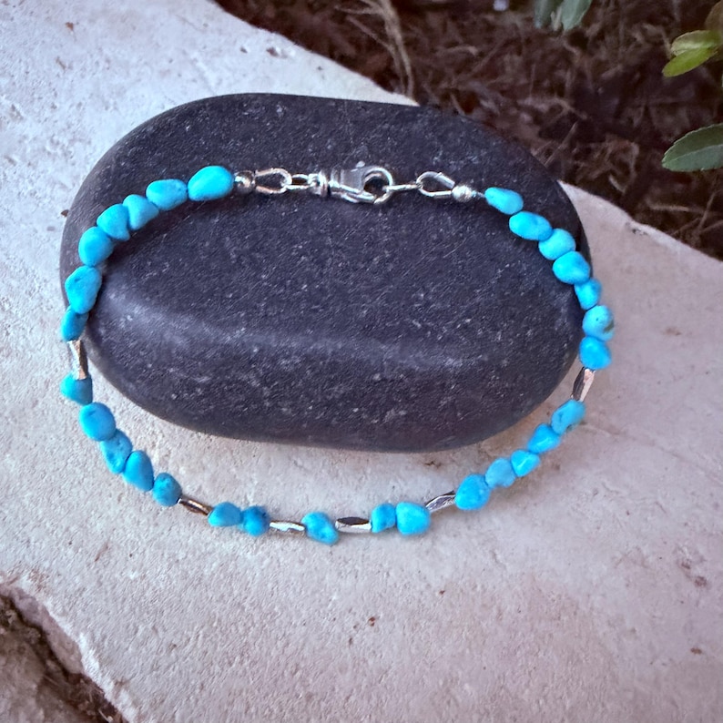May include: A bracelet featuring small, irregular, bright turquoise-colored stone beads interspersed with thin, cylindrical silver-toned metal spacers. The piece is secured with a silver-toned lobster claw clasp and jump ring closure.
