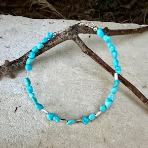 May include: A bracelet featuring small, irregular, bright turquoise-colored stone beads interspersed with thin, cylindrical silver-toned metal spacers. The piece is finished with a silver-toned metal lobster claw clasp and a short extender chain.