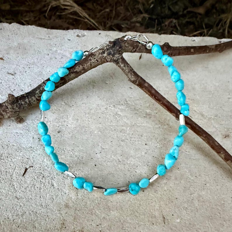 May include: A bracelet featuring small, irregular, bright turquoise-colored stone beads interspersed with thin, cylindrical silver-toned metal spacers. The piece is finished with a silver-toned metal lobster claw clasp and a short extender chain.