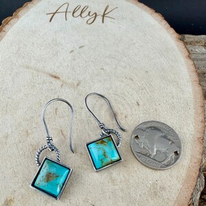 May include: Silver-toned earrings with square turquoise stones. The turquoise stones are set in a silver frame and have a twisted silver accent. A silver coin with a buffalo image is next to the earrings. The text "Allyk" is at the top.