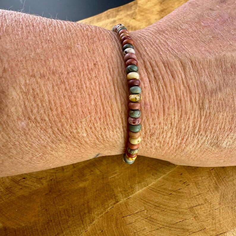 May include: A beaded bracelet featuring a variety of earth-toned beads, including shades of brown, beige, green, and red. The bracelet is strung on a flexible cord and is approximately 7 inches in circumference.
