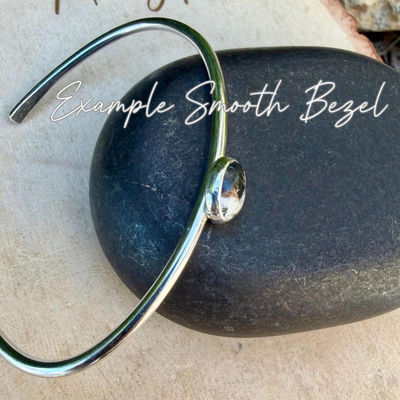 May include: A silver-toned bracelet with a smooth bezel design. The bracelet features a clear, round gemstone set in a silver bezel. The words "Example Smooth Bezel" are written in white script across the image.