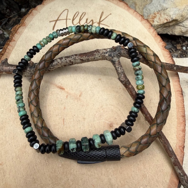 May include: A handcrafted bracelet featuring a braided brown leather band and a strand of black beads interspersed with turquoise-colored stones. The bracelet has a black magnetic clasp and the word "Allyk" is visible in the background.