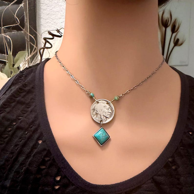 Op de afbeelding: Zilveren ketting met een vintage buffel nikkel hanger en een turquoise diamantvormige steen. De ketting heeft een fijne ketting met kleine turquoise kralen. De hanger is gecentreerd op de borst.