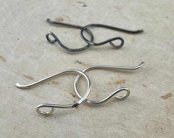 May include: Two pairs of handcrafted earrings. One pair is silver-toned, and the other is a darker, possibly oxidized, metal. Both pairs feature a looped design with a curved hook for the ear.